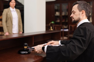 Photo of Judge striking gavel at wooden table in courtroom, selective focus