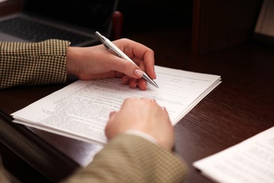 Photo of Notary signing document at wooden table, closeup