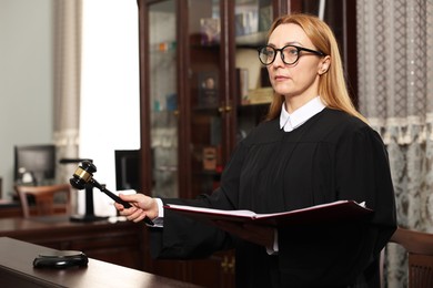 Judge with folder of documents striking gavel at table in courtroom