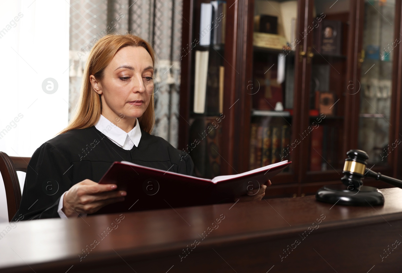 Photo of Judge with folder of documents at wooden table in courtroom