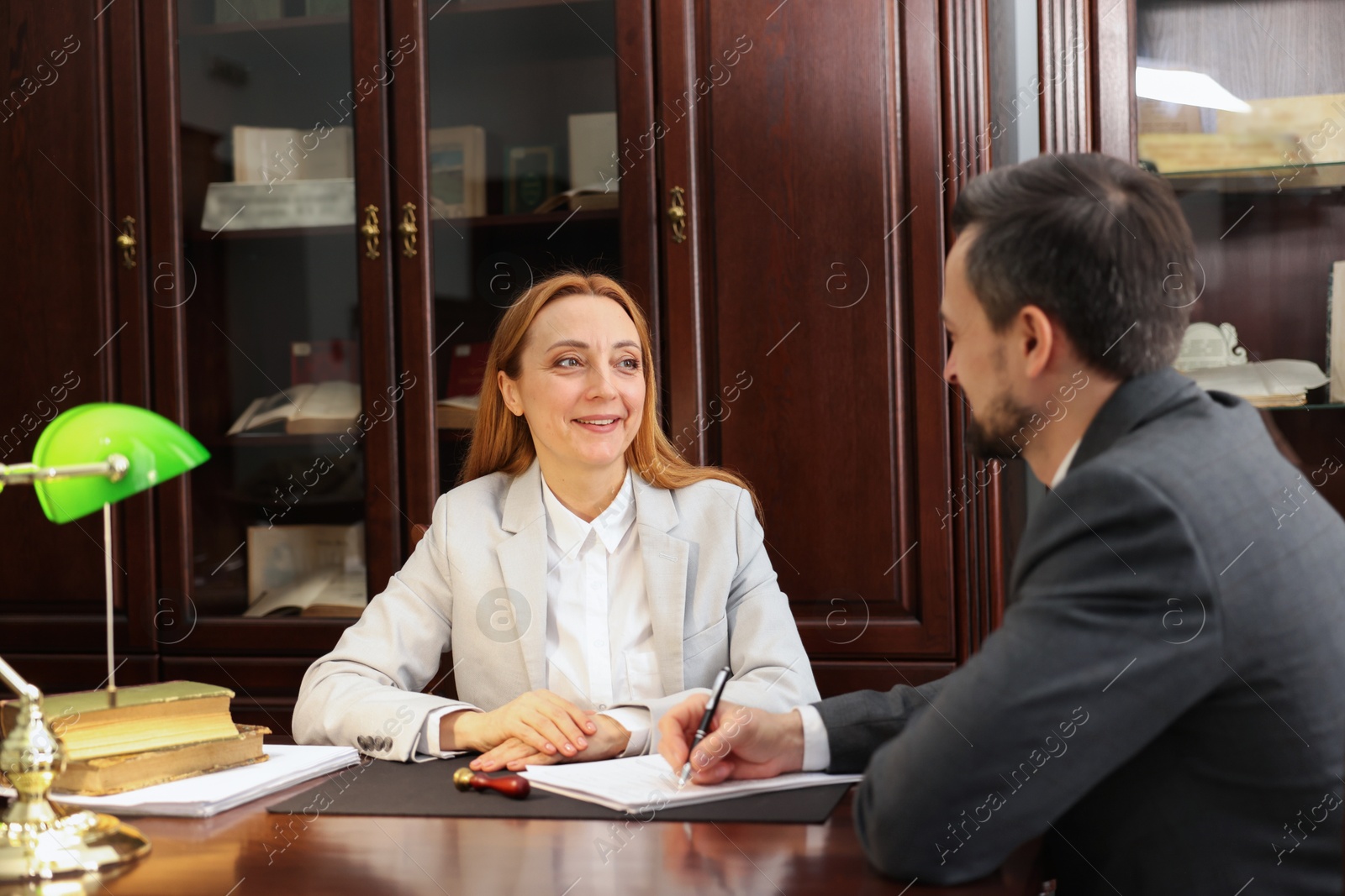 Photo of Smiling notary working with client at table in office