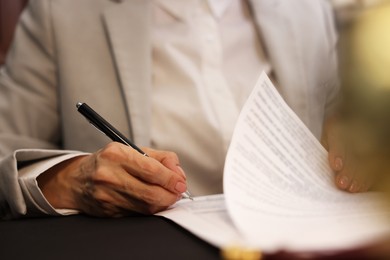 Photo of Notary signing document at table in office, closeup