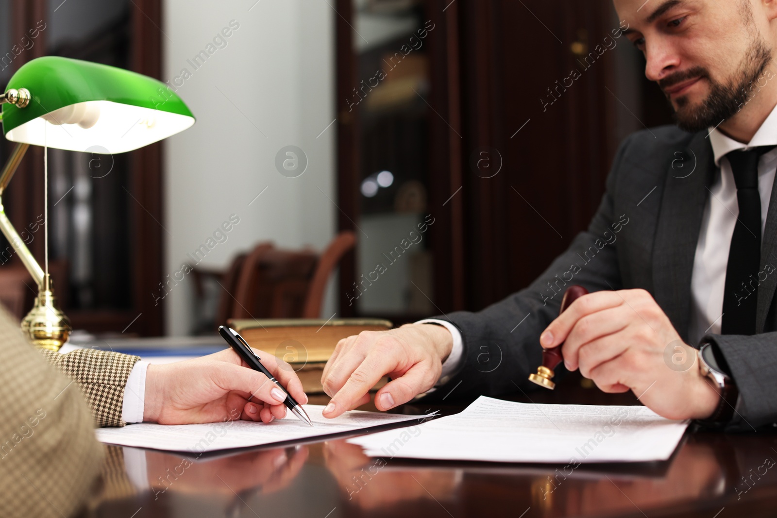 Photo of Notary showing client where to sign document at table in office, closeup