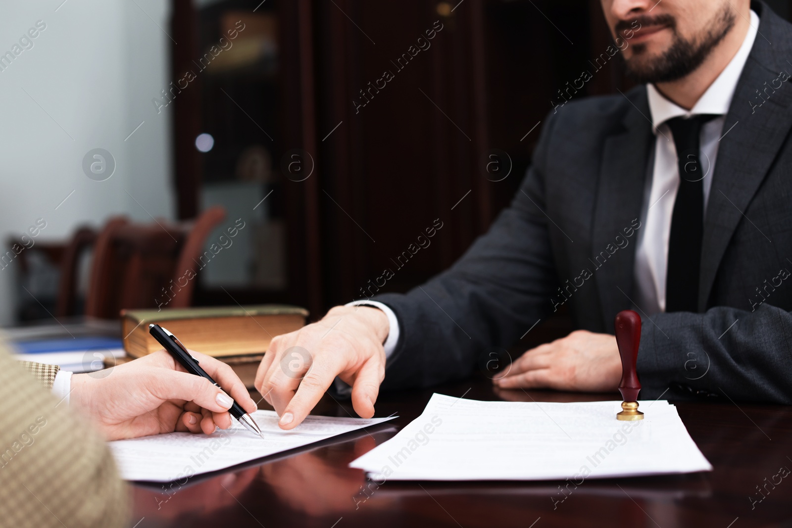 Photo of Notary showing client where to sign document at table in office, closeup