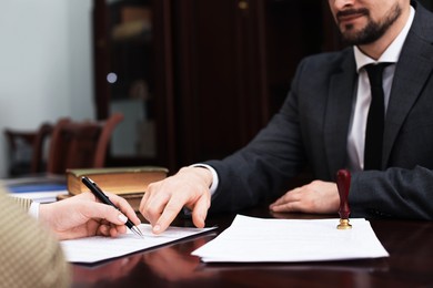 Notary showing client where to sign document at table in office, closeup