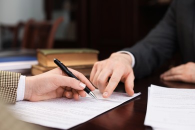 Notary showing client where to sign document at table in office, closeup