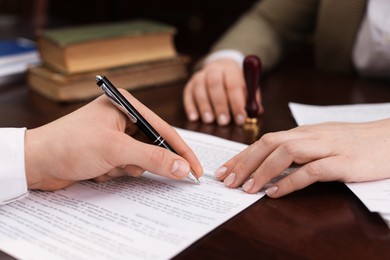 Photo of Notary and client signing document at table in office, closeup