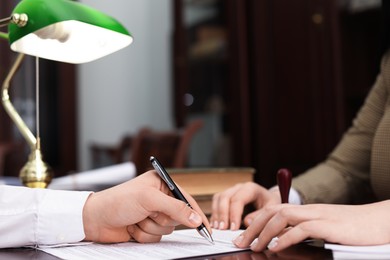 Notary and client signing document at table in office, closeup