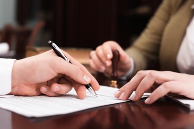 Photo of Notary and client signing document at table in office, closeup