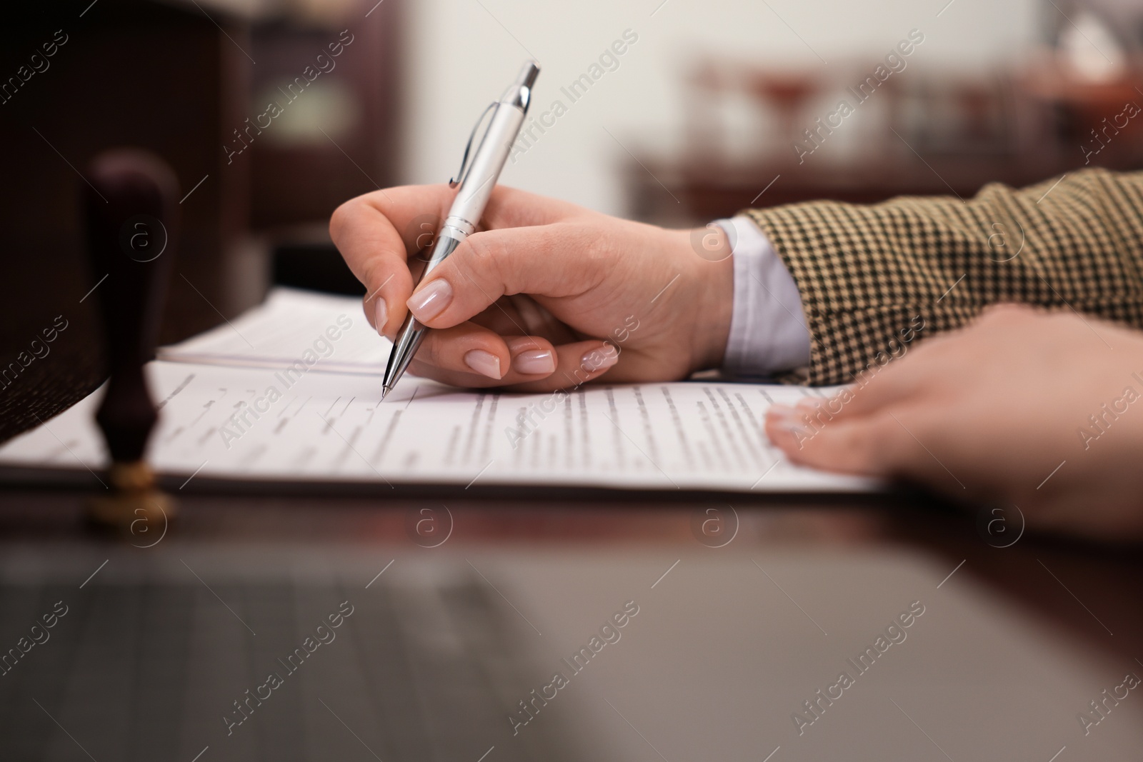 Photo of Notary signing document at table in office, closeup