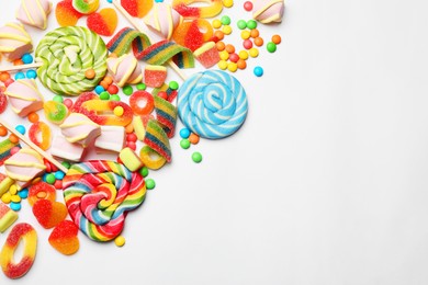 Photo of Many different tasty candies and marshmallows on white background, flat lay. Space for text