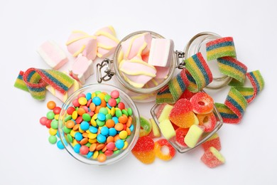 Many different tasty candies and marshmallows on white background, flat lay