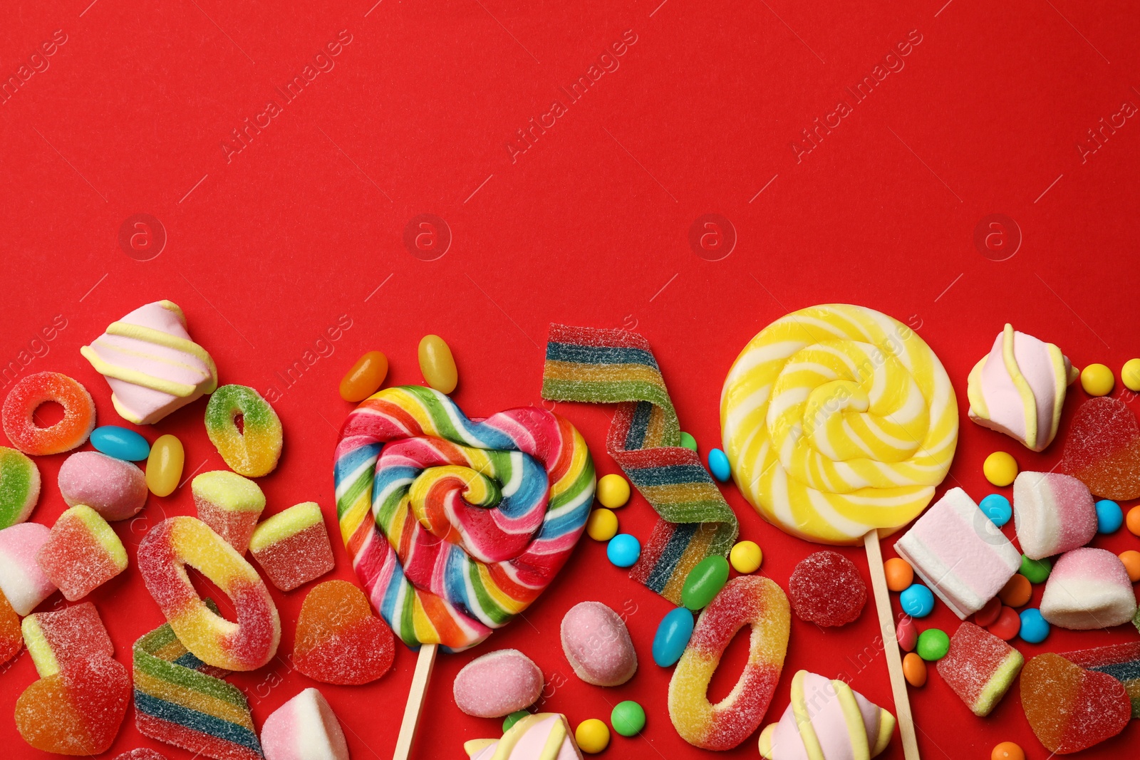 Photo of Different delicious candies and marshmallows on red background, flat lay. Space for text