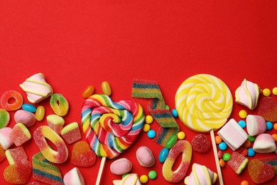 Different delicious candies and marshmallows on red background, flat lay. Space for text