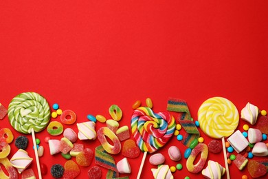 Different delicious candies and marshmallows on red background, flat lay. Space for text