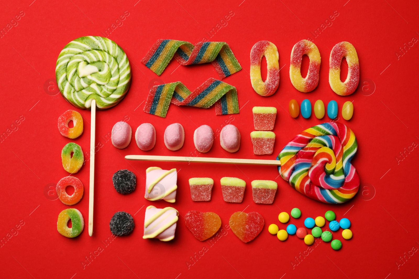 Photo of Different delicious candies and marshmallows on red background, flat lay