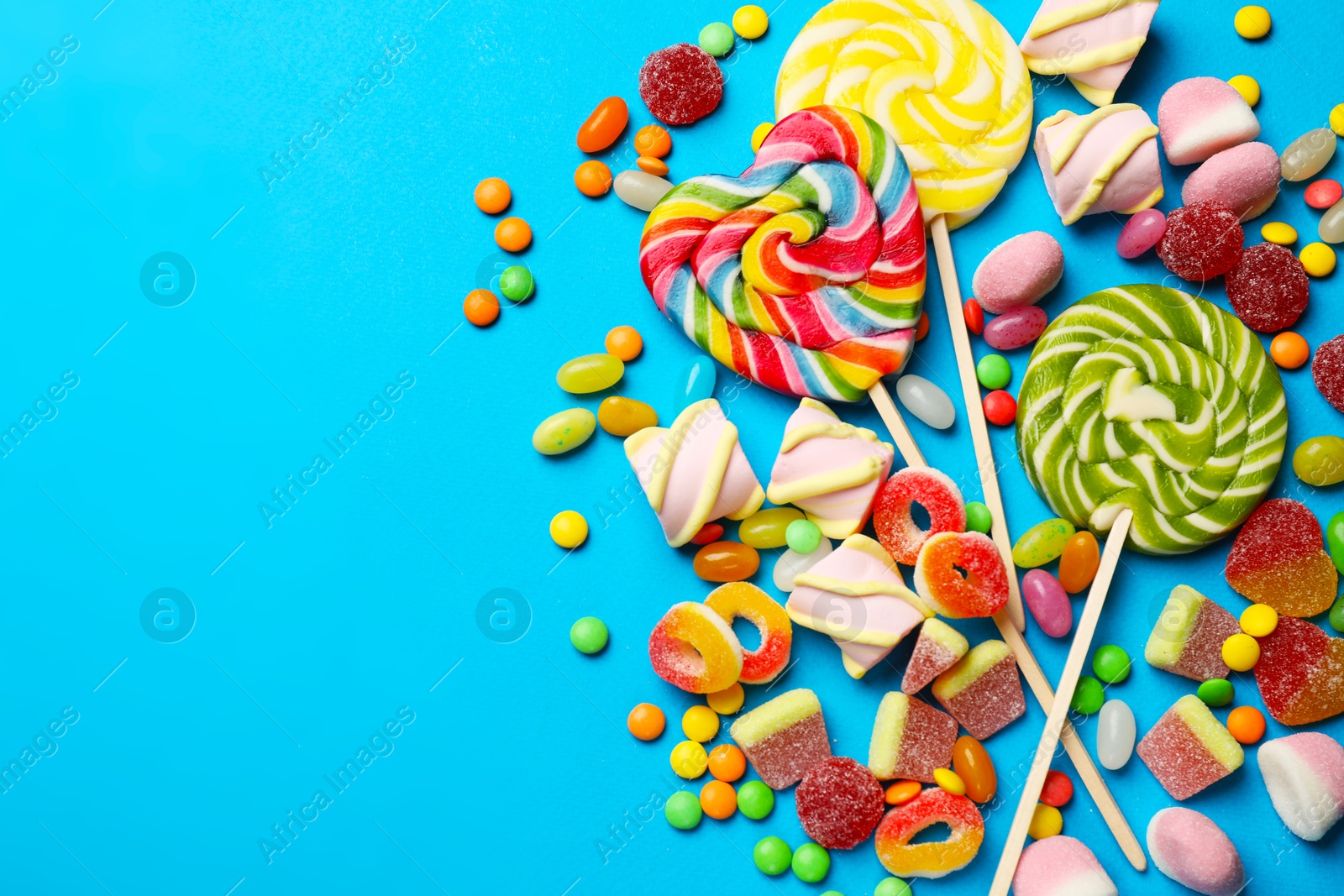 Photo of Different delicious candies and marshmallows on blue background, flat lay. Space for text