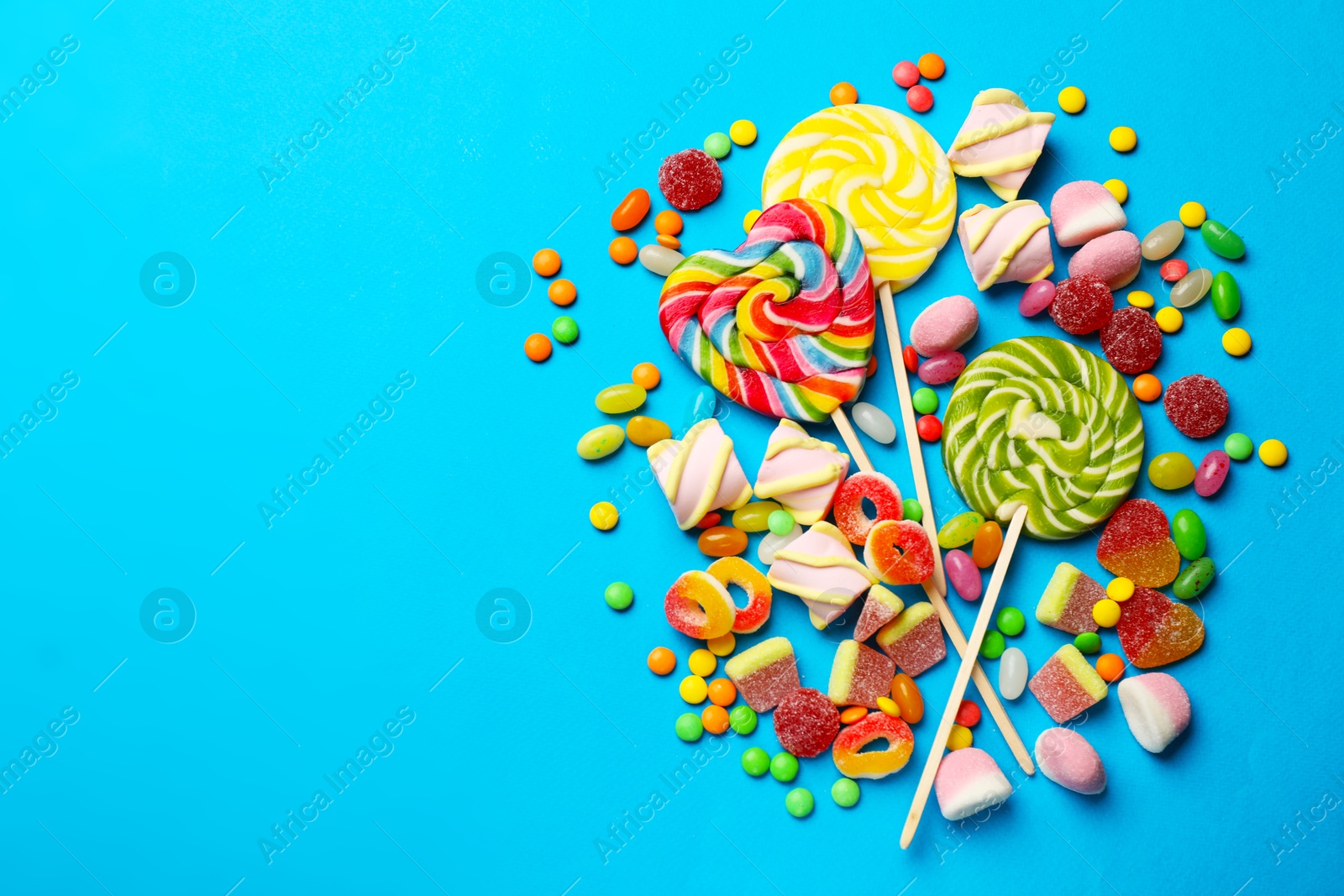 Photo of Different delicious candies and marshmallows on blue background, flat lay. Space for text