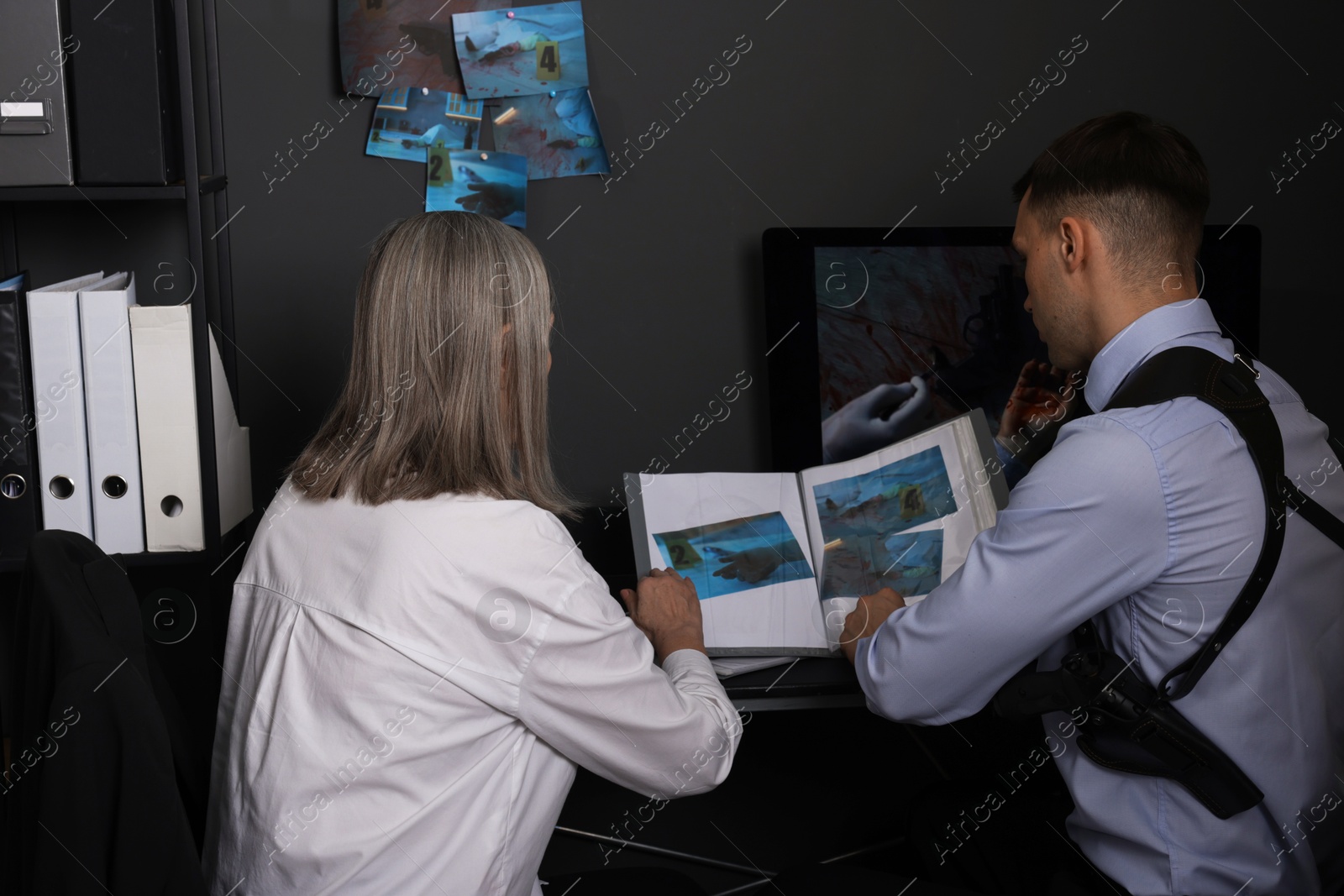 Photo of Forensic experts working with crime scene photos in office, back view