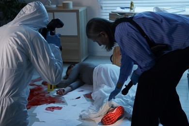 Photo of Forensic experts working at crime scene with dead woman's body indoors