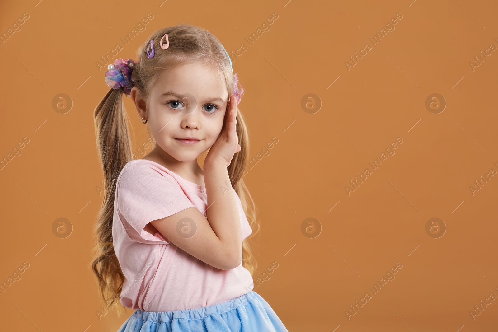 Photo of Cute little girl wearing beautiful hair accessories on light brown background. Space for text