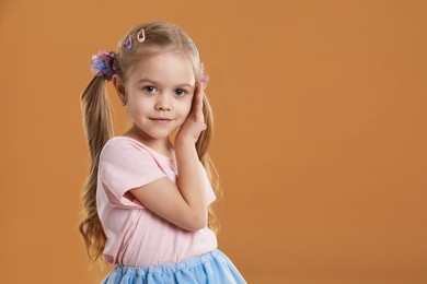 Photo of Cute little girl wearing beautiful hair accessories on light brown background. Space for text