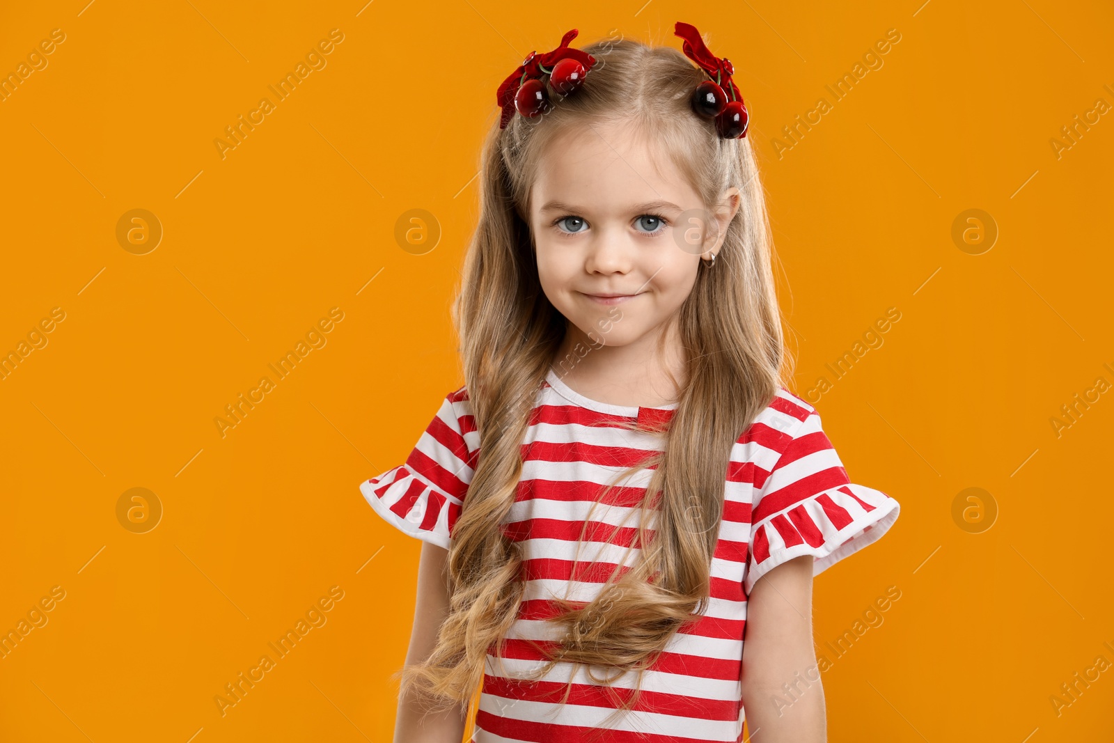 Photo of Cute little girl wearing beautiful bows with cherries on orange background