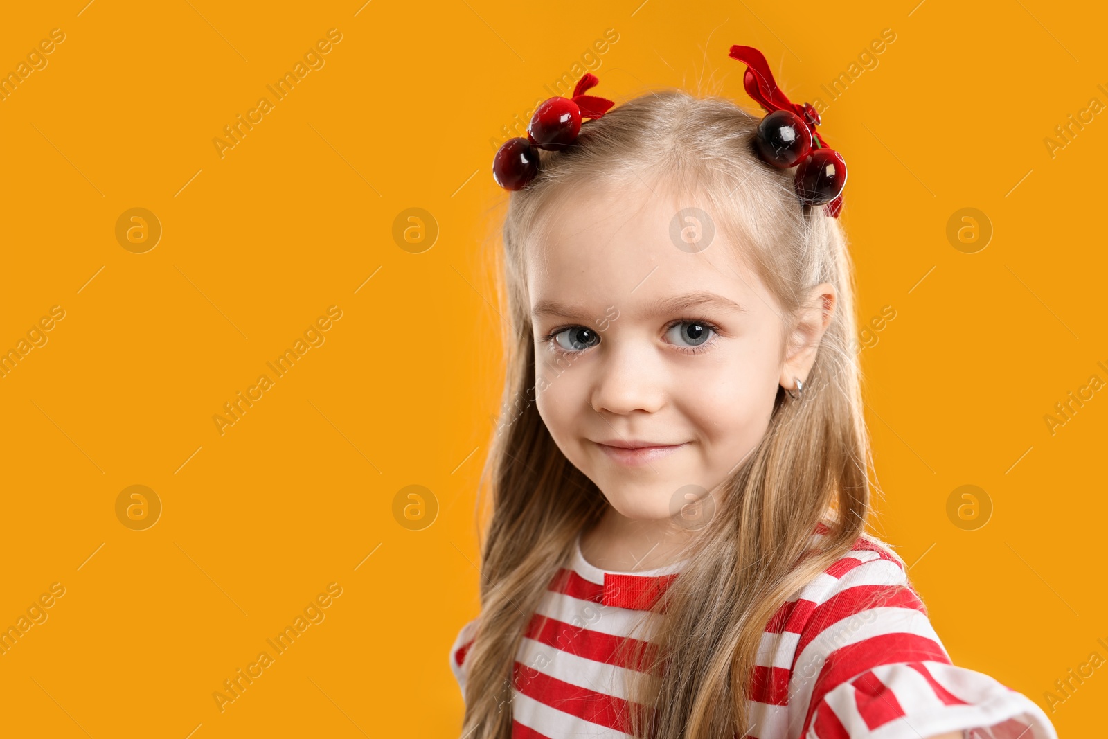 Photo of Cute little girl with beautiful hair clips taking selfie on orange background