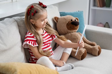 Photo of Cute little girl wearing beautiful bows with cherries on sofa at home