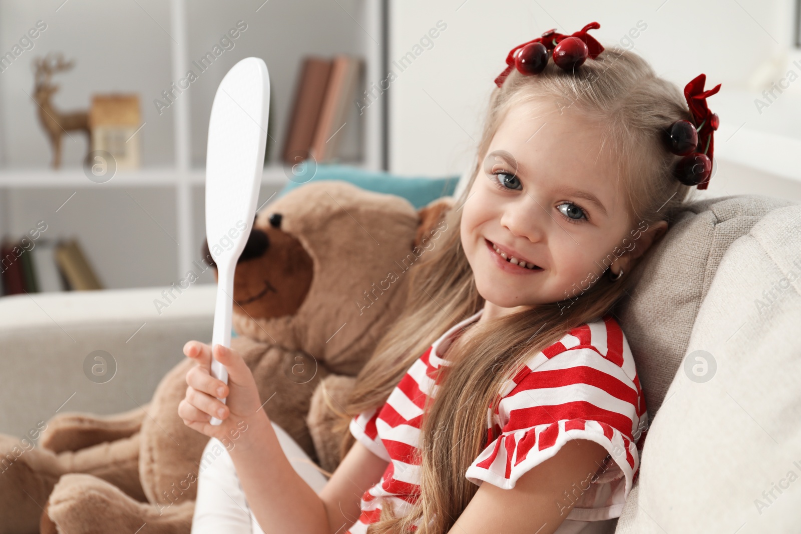 Photo of Cute little girl with beautiful hair clips looking into mirror at home