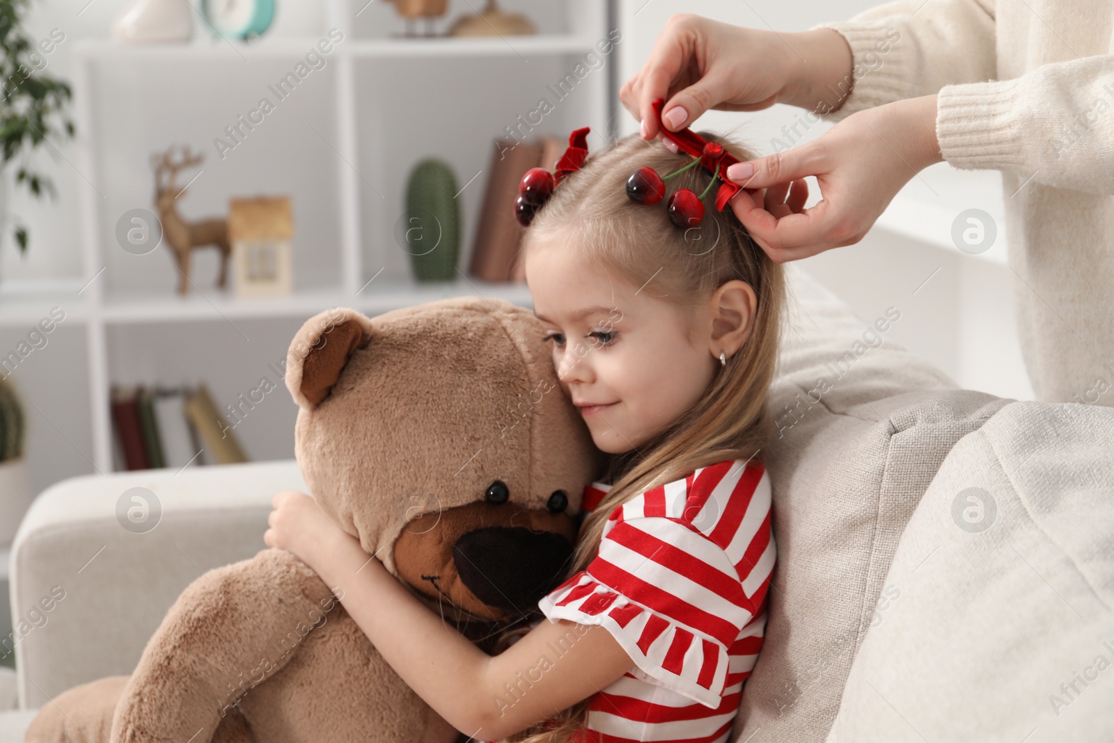 Photo of Mom putting cute accessories onto her daughter's hair at home, closeup