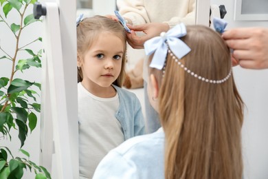 Photo of Mom putting cute accessories onto her daughter's hair at home, closeup