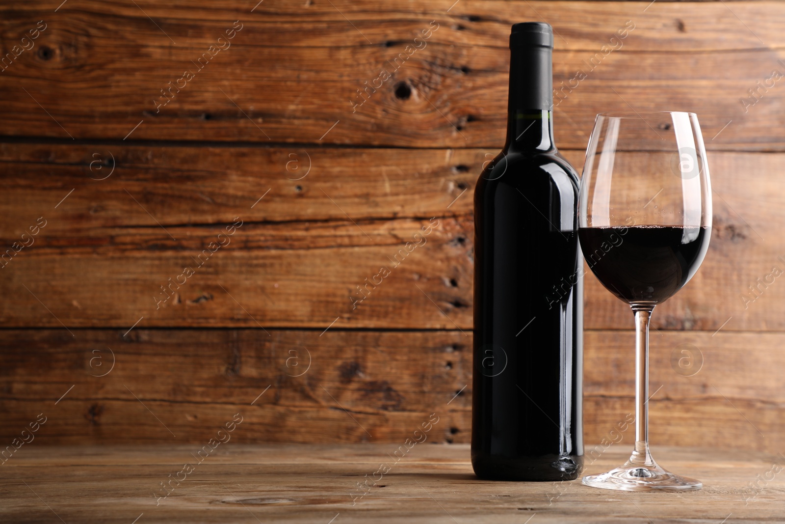 Tasty red wine in glass and bottle on wooden table, space for text Photo of Tasty red wine in glass and bottle on wooden table, space for text