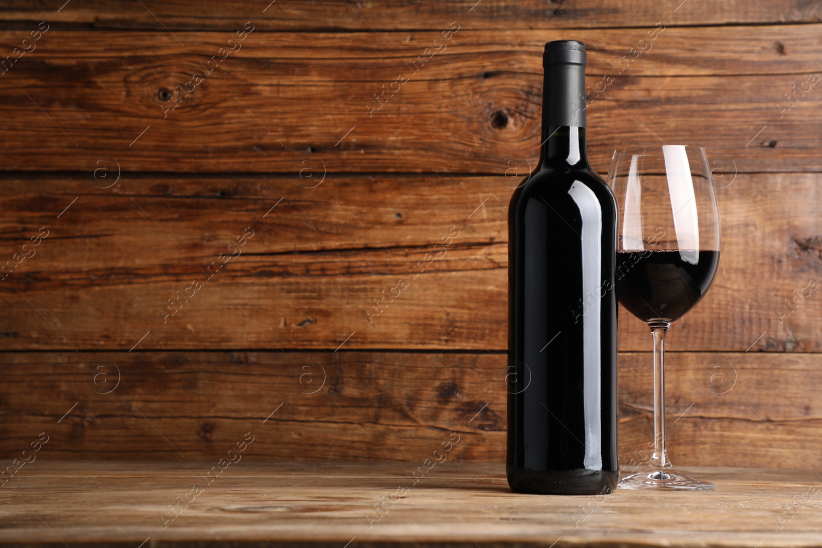 Photo of Tasty red wine in glass and bottle on wooden table, space for text
