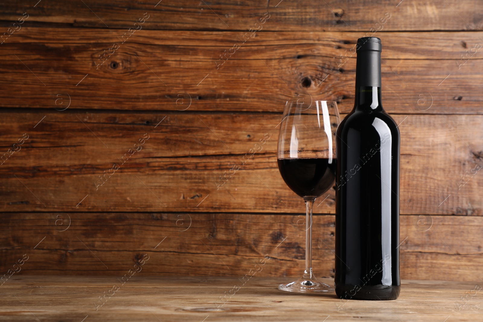 Tasty red wine in glass and bottle on wooden table, space for text Photo of Tasty red wine in glass and bottle on wooden table, space for text