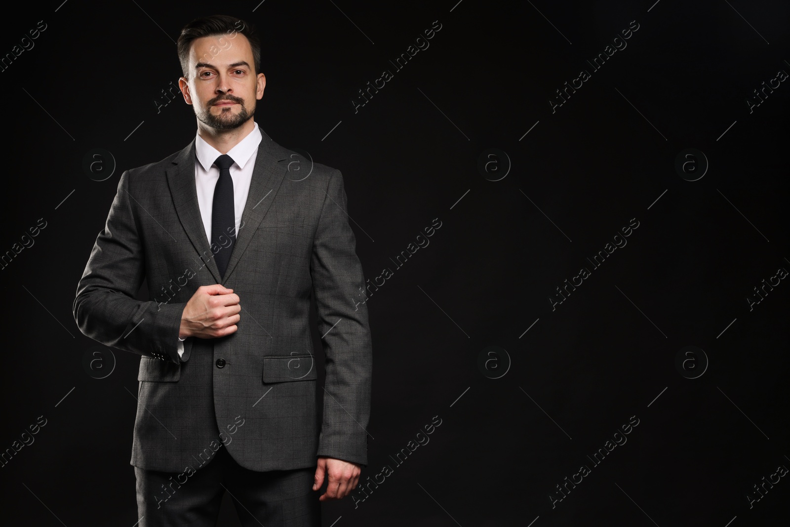 Photo of Confident man in classic suit on black background. Space for text