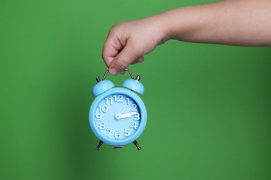 Photo of Child holding light blue alarm clock on green background