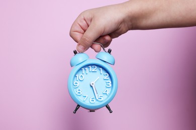 Photo of Child holding light blue alarm clock on pink background