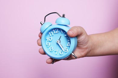 Photo of Child holding light blue alarm clock on pink background