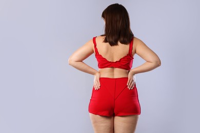 Photo of Woman in red underwear on light grey background, back view. Cellulite problem