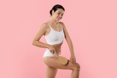 Photo of Woman doing anti cellulite massage with brush on pink background