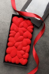 Photo of Chocolate bar decorated with hearts in box and red ribbon on grey table, flat lay