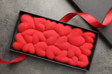 Photo of Chocolate bar decorated with hearts in box and red ribbon on grey table, flat lay