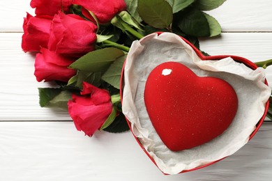 Photo of Heart shaped chocolate in box and red roses on white wooden table, flat lay