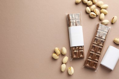 Photo of Delicious Dubai chocolate bars and pistachios on beige background, flat lay. Space for text