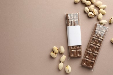 Photo of Delicious Dubai chocolate bars and pistachios on beige background, flat lay. Space for text