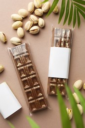 Photo of Delicious Dubai chocolate bars, pistachios and leaves on beige background, flat lay