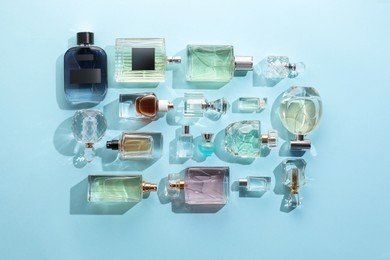 Photo of Bottles of various perfumes on light blue background, flat lay