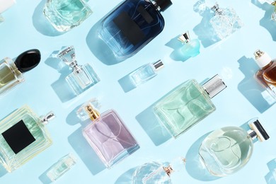 Photo of Bottles of various perfumes on light blue background, flat lay