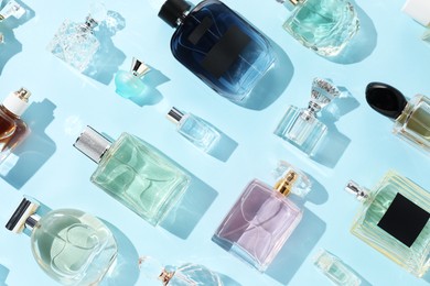 Photo of Bottles of various perfumes on light blue background, flat lay